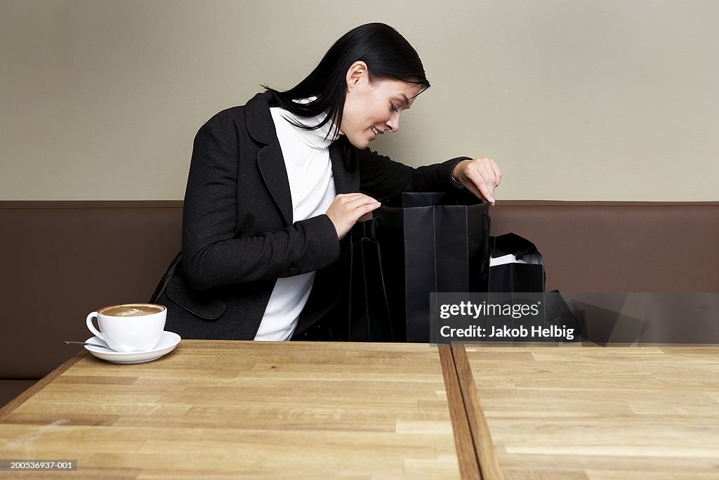Young woman sitting in cafe looking in shopping bag, smiling
