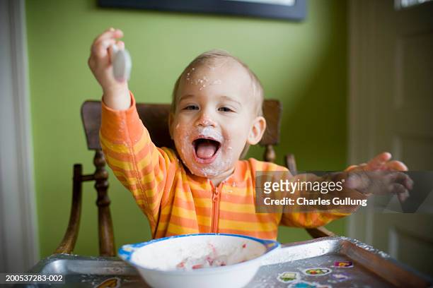 baby boy (15-18 months) in high chair, face covered with food, smiling - baby eating food imagens e fotografias de stock