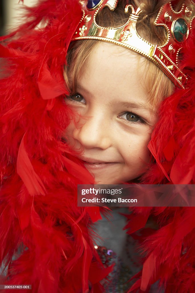 Girl (6-8) wearing crown and red feather boa, smiling, close-up