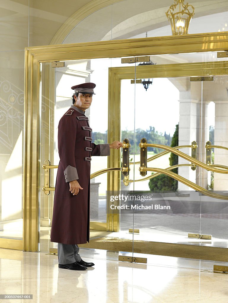 Concierge holding door in hotel foyer, portrait