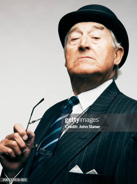 senior businessman wearing hat, holding glasses, close-up, portrait - smug 個照片及圖片檔
