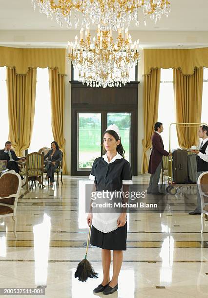 maid holding feather duster standing under chandelier in hotel foyer - 30 40 woman stockfoto's en -beelden