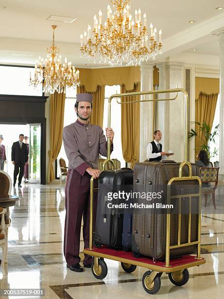 bellboy holding luggage trolley in hotel foyer, portrait - luggage trolley stockfoto's en -beelden