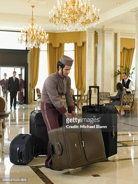 bellboy lifting heavy suitcases in hotel foyer - bellhop stockfoto's en -beelden