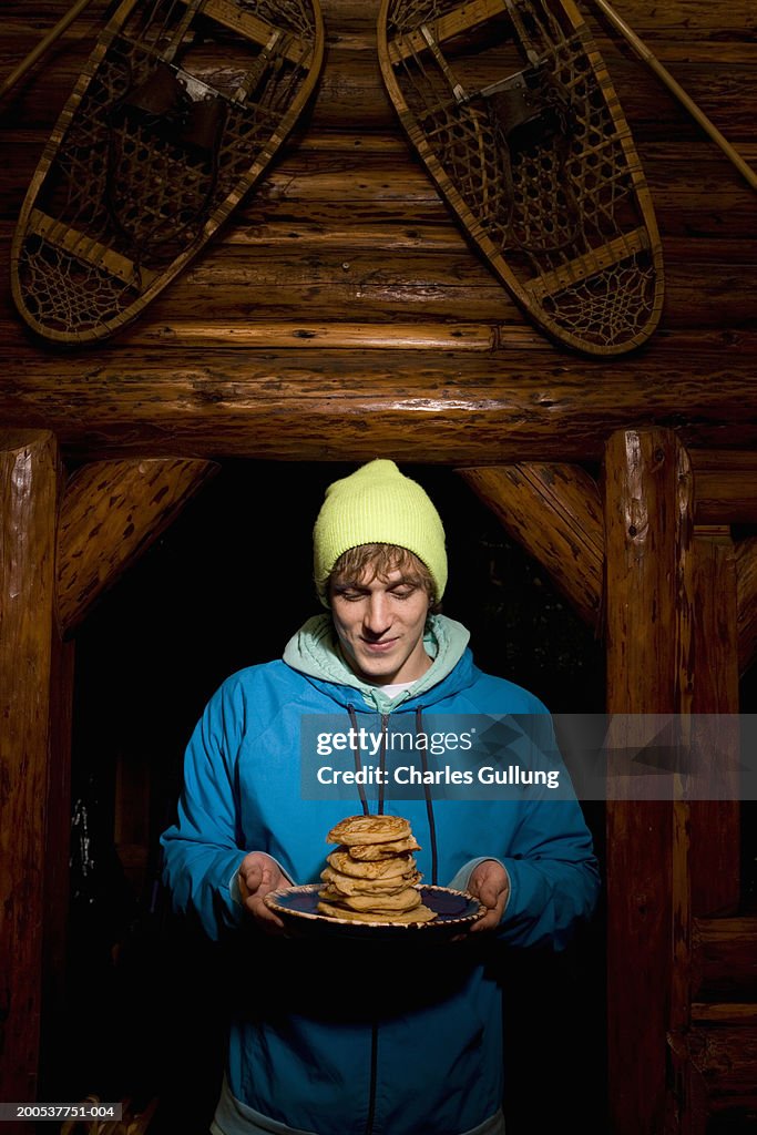 Young man holding plate of pancakes in log cabin