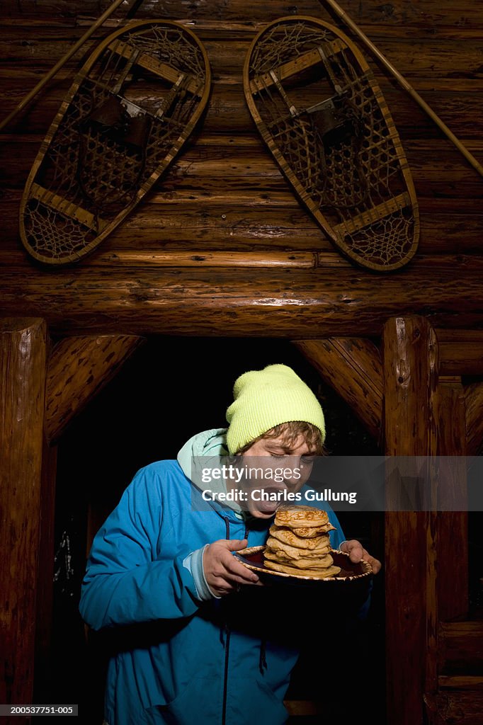 Young man holding plate of pancakes in log cabin
