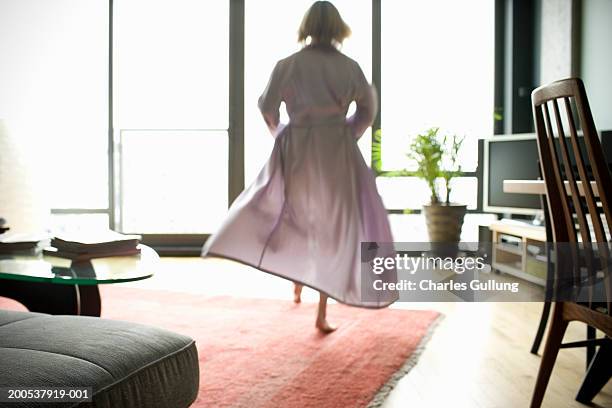 mature woman in bathrobe walking across living room, rear view - bathrobe stockfoto's en -beelden