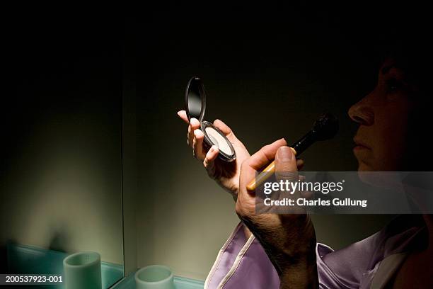 mature woman applying make-up in compact mirror, side view - compact mirror stockfoto's en -beelden