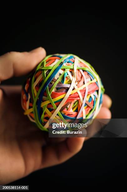 man holding rubber band ball, against black background, close-up - elastic band ball ストックフォトと画像