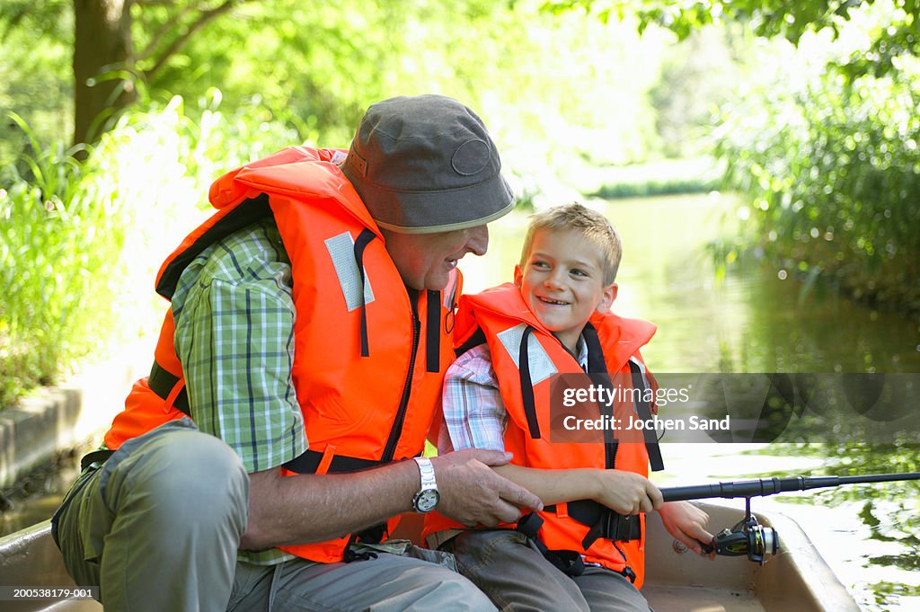 Grandfather and grandson (6-8) fishing from boat, smiling