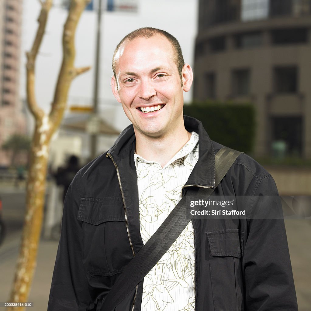 Young man standing on sidewalk, smiling