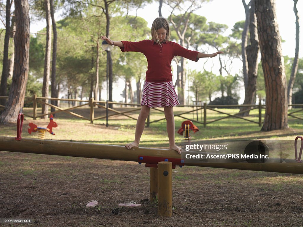 Girl (10-12) balancing atop seesaw, arms outstretched