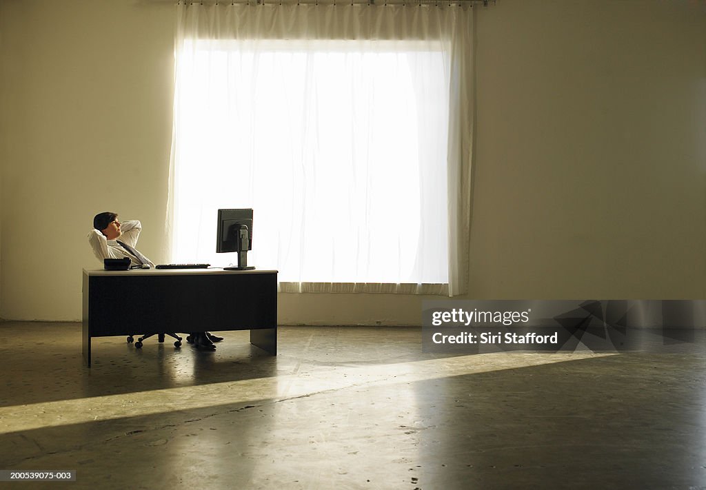 Businessman sitting at desk, hands behind head