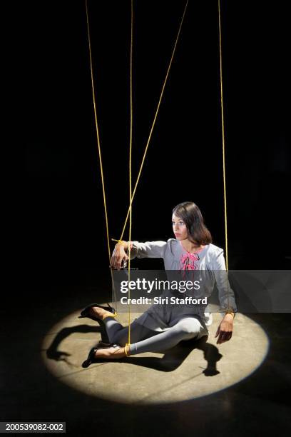 woman tied in strings sitting on floor with spotlight - marionetta foto e immagini stock