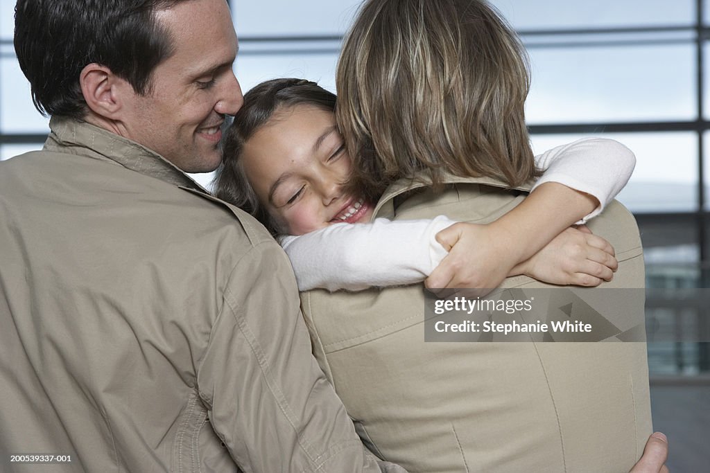 Girl (5-7) embracing parents in airport, rear view