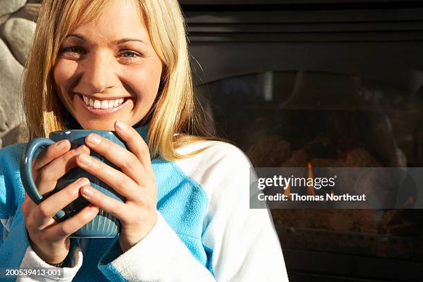 woman holding coffee cup beside fireplace, smiling, portrait - après ski stock-fotos und bilder