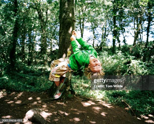 boy (5-7) swinging on rope hanging from tree in woodland - schommelen bungelen stockfoto's en -beelden