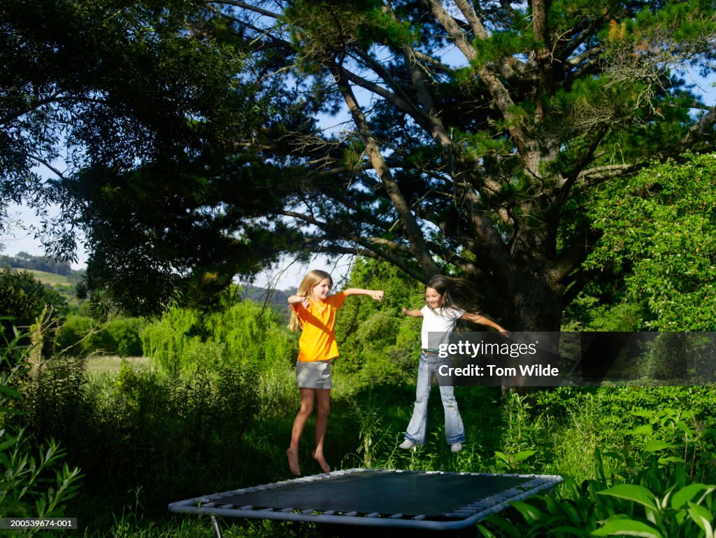 Two girls (10-12) playing on trampoline in garden