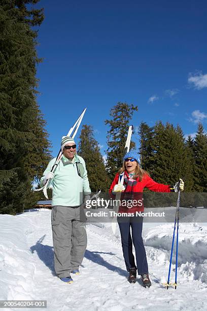 mature man and woman carrying cross-country skis, laughing - langlaufski stock-fotos und bilder