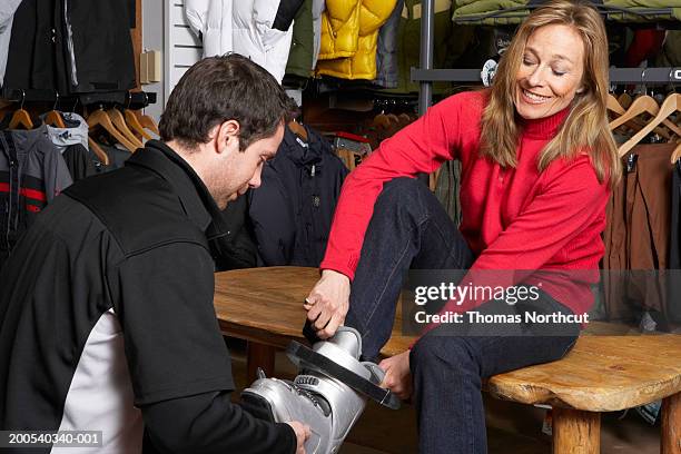 salesman helping mature woman try on ski boots in sports shop - skischoen stockfoto's en -beelden