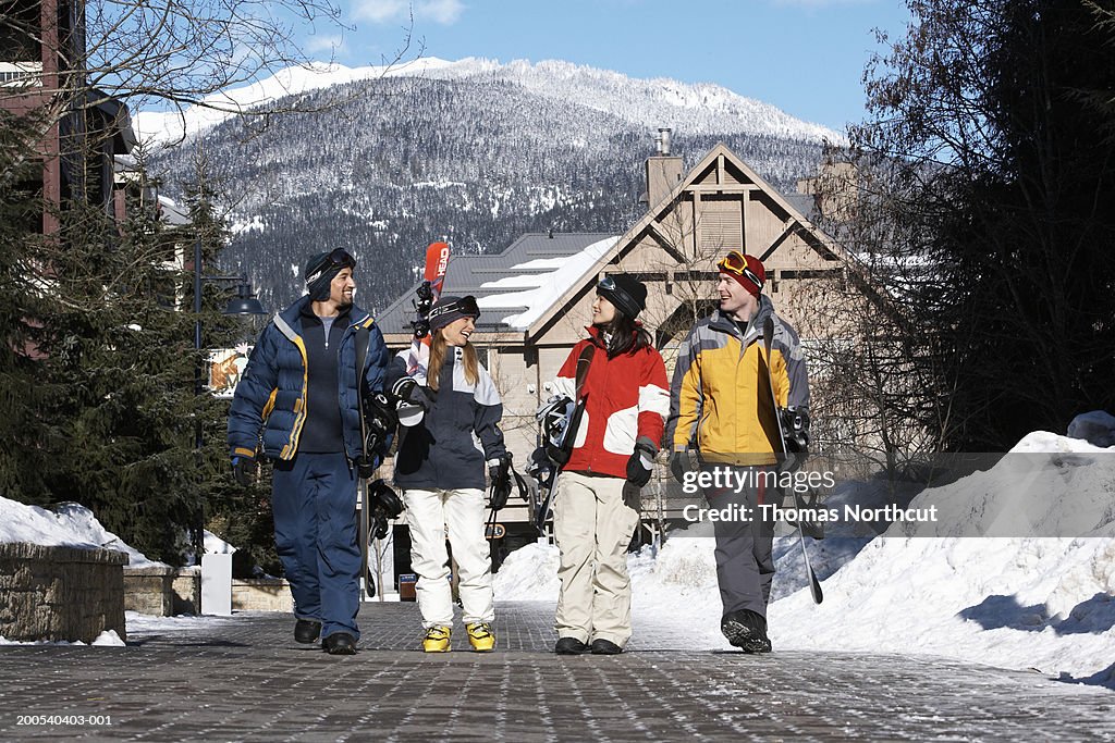 Four adults with skis and snowboards walking and talking