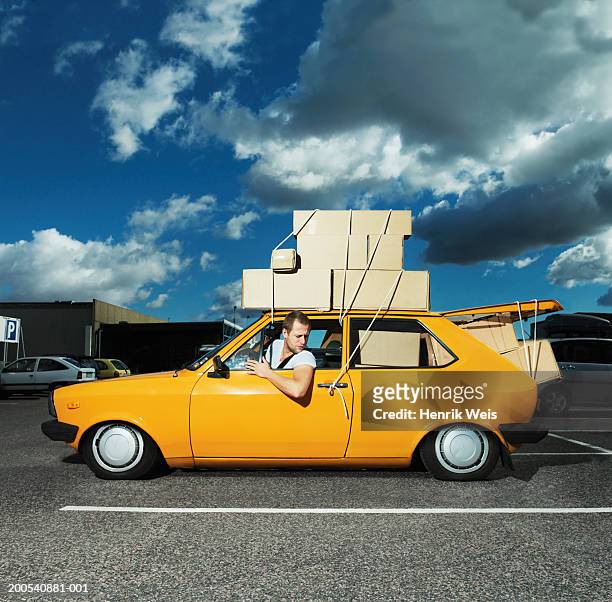 man in yellow car filled with boxes and tied to roof - over burdened stock pictures, royalty-free photos & images