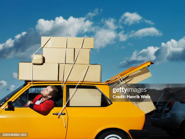 man in yellow car filled with boxes looking up at boxes tied to roof - over burdened stock pictures, royalty-free photos & images