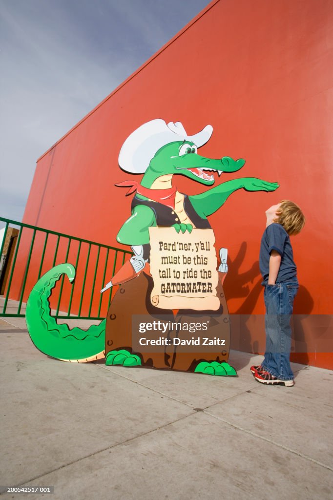 Boy standing next to carnival ride sign indicating height requirement