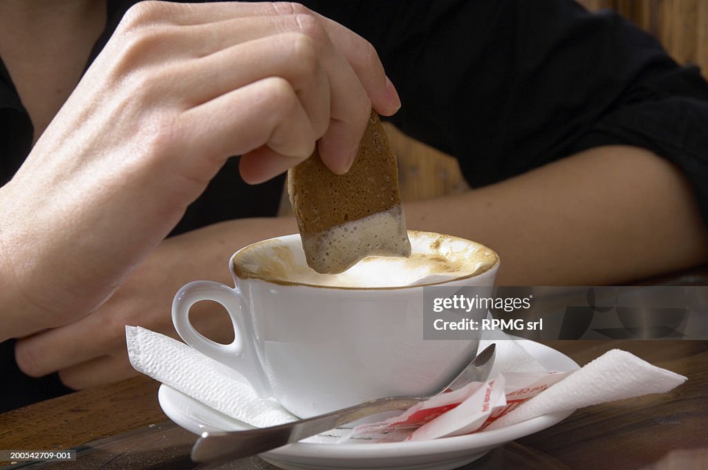 Woman dipping bisuit into coffee, close-up