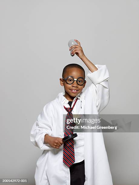 boy (5-7) in lab coat, holding light bulb and magnifying glass - inventor fotografías e imágenes de stock