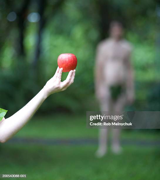 woman holding apple in forest, man in background (focus on apple) - adam und eva stock-fotos und bilder