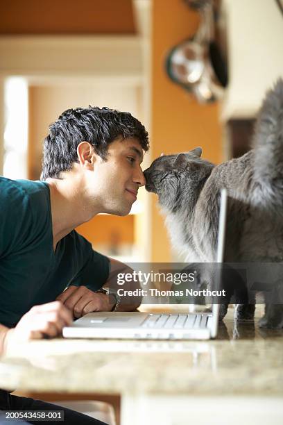 jeune homme avec ordinateur portable et le chat nez à nez, vue latérale - pet owner photos et images de collection