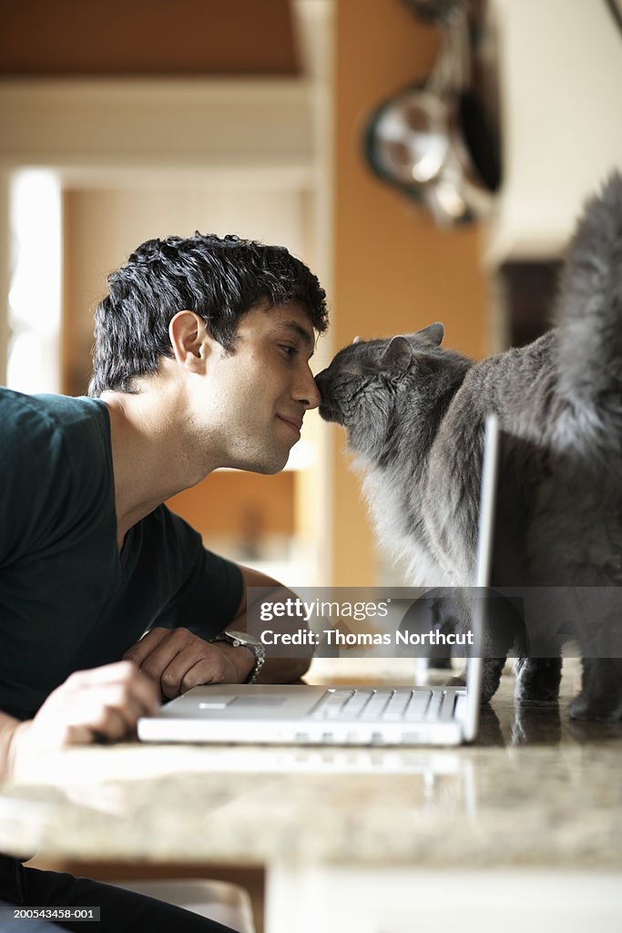 Young man with laptop and cat nose to nose, side view