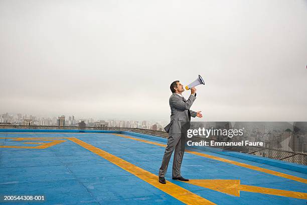 business man standing on heliport overlooking city, with megaphone - megaphone - fotografias e filmes do acervo