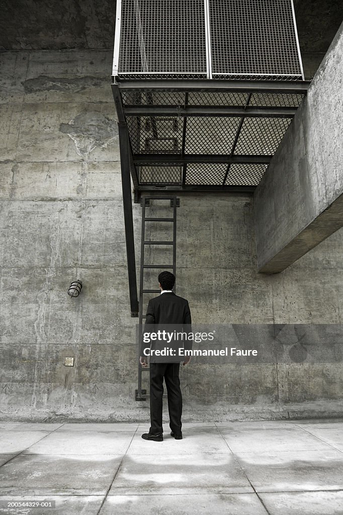 Man in suit standing by ladder in concrete area, rear view