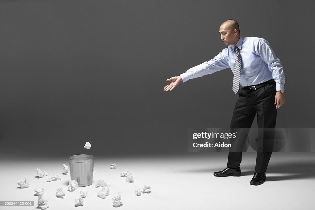 Man throwing crumpled paper into waste basket, studio shot