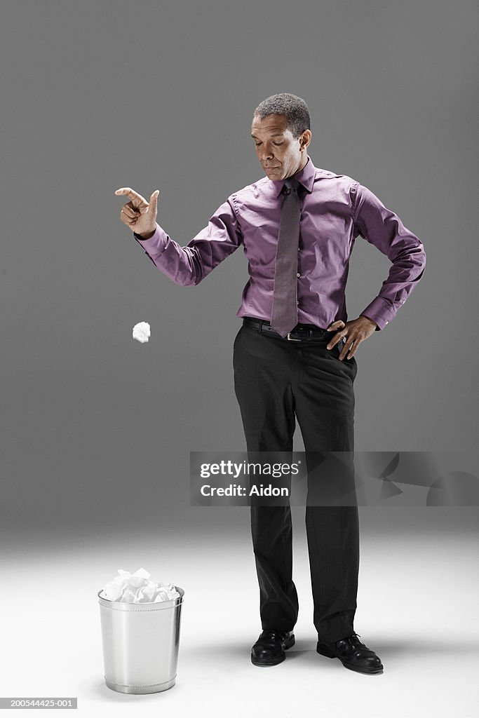 Businessman dropping crumpled paper into waste basket, studio shot