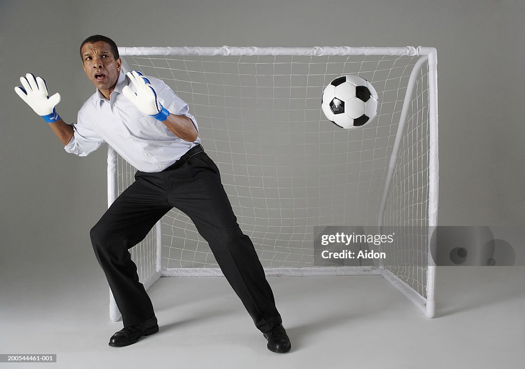 Businessman playing goalkeeper, missing ball, studio shot