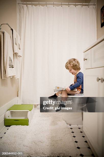 boy (2-4) sitting on toilet, looking at magazine, side view - childrens closet stockfoto's en -beelden