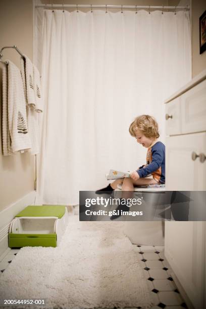 boy (2-4) sitting on toilet, looking at magazine, side view - potty training stock pictures, royalty-free photos & images