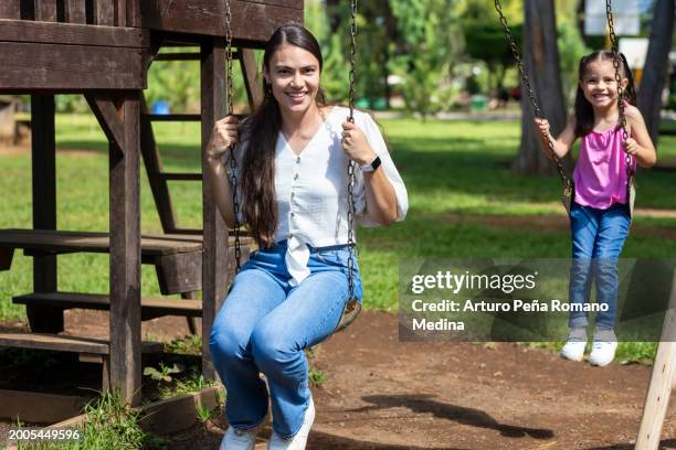 mum accompanying her little girl on the swings - accompanying stock pictures, royalty-free photos & images