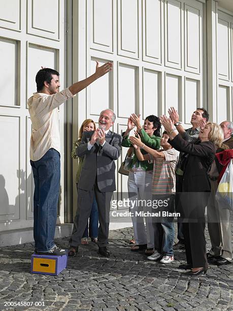 man standing on box in street holding out arms to applauding crowd - omgeven stockfoto's en -beelden