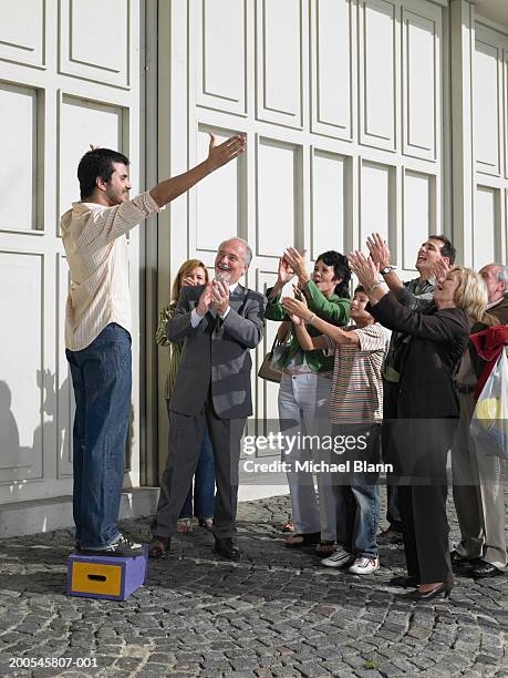 man standing on box in street holding out arms to applauding crowd - applause stock pictures, royalty-free photos & images