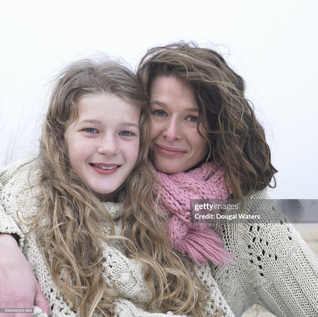 Mother and daughter (8-10) embracing on beach, smiling, close-up