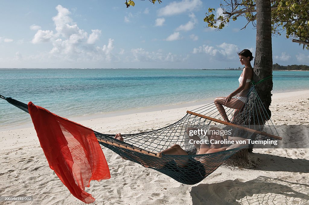 Man relaxing in hammock, woman leaning against palm tree