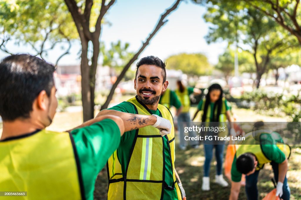 Mid adult recycler man greeting other recycler and cleaning the public park