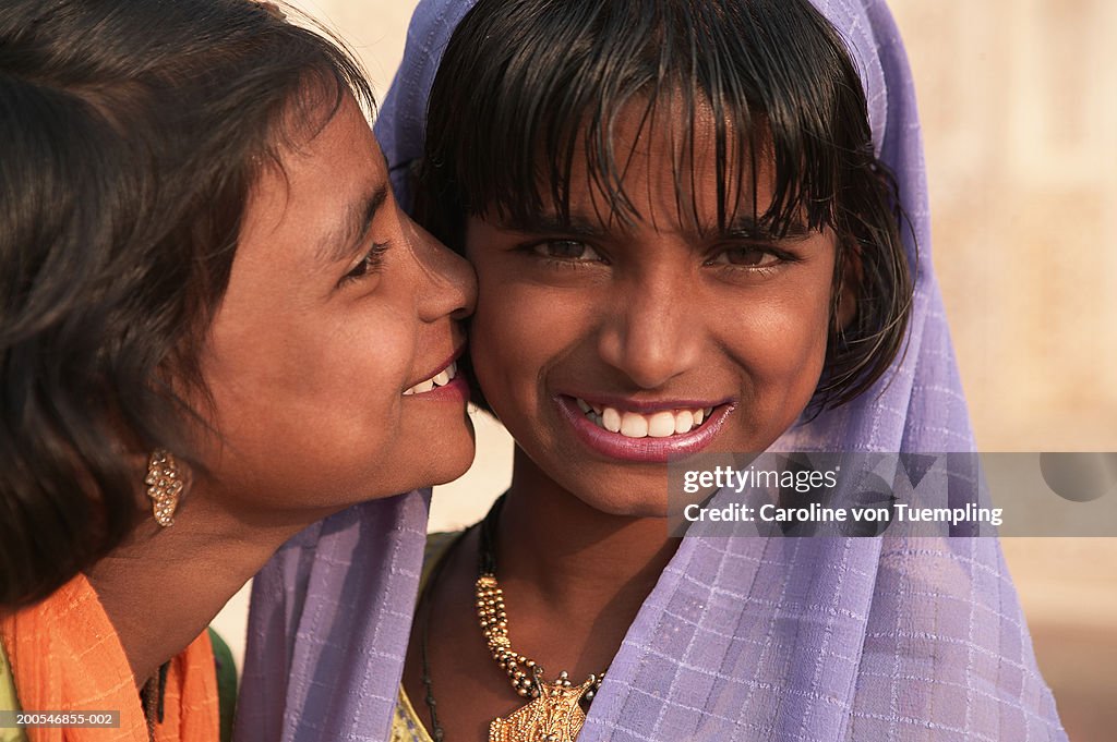 Girl kissing on sister's (11-14) cheek smiling, close-up