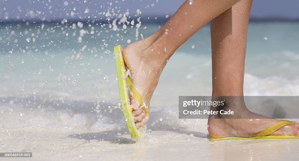 Young woman wearing flip-flops walking on beach, low section