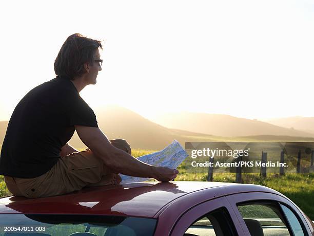 man sitting on car roof, holding map - sitting on top of car stock pictures, royalty-free photos & images