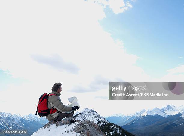 mountaineer sitting on mountain top, holding map - climbing plant stock-fotos und bilder